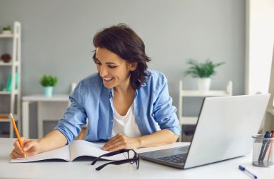 A woman in front of her computer and writing in a notebook.